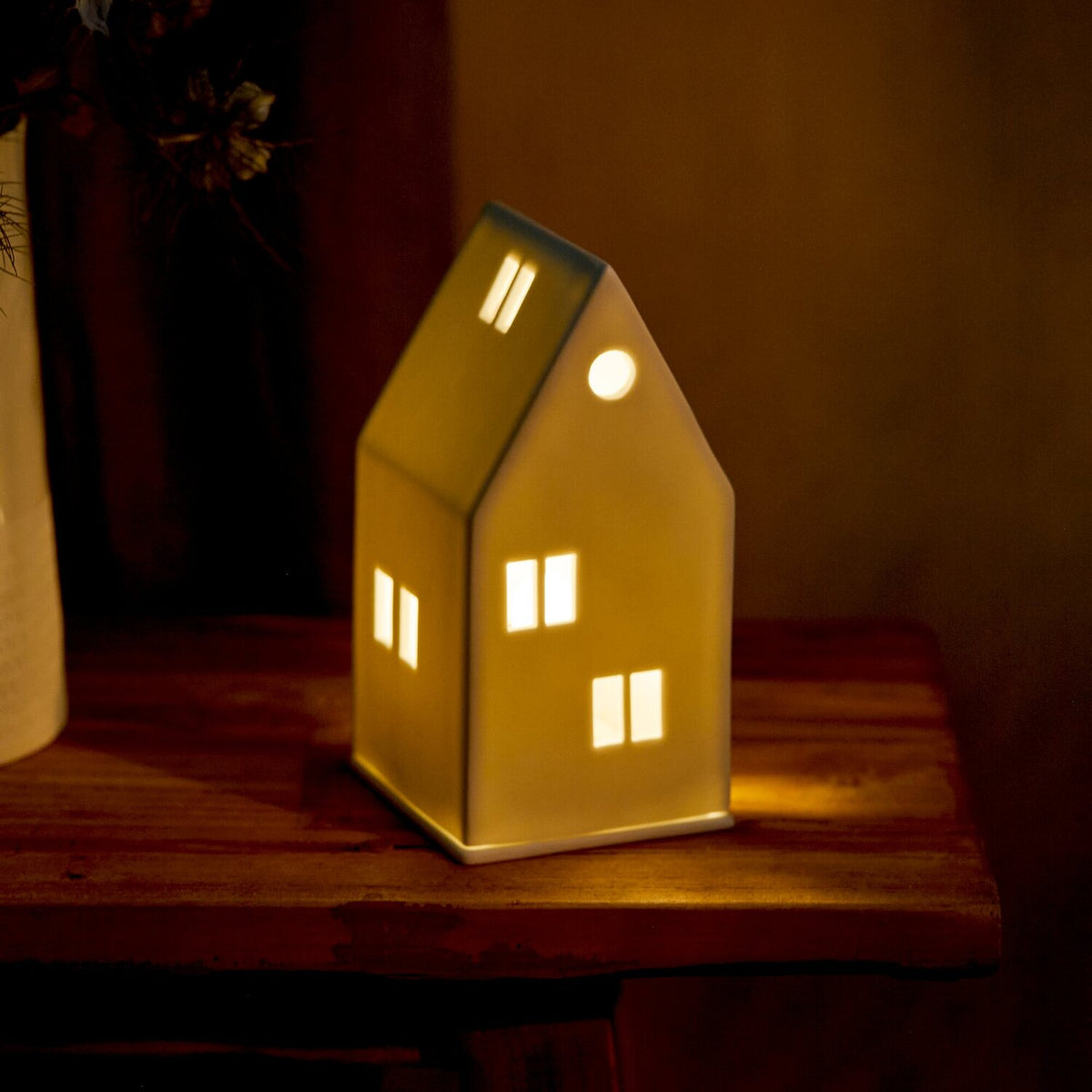 Weißes Lichthaus mit Satteldach, warmes Licht durch Fensteröffnungen, kompakte Standform
