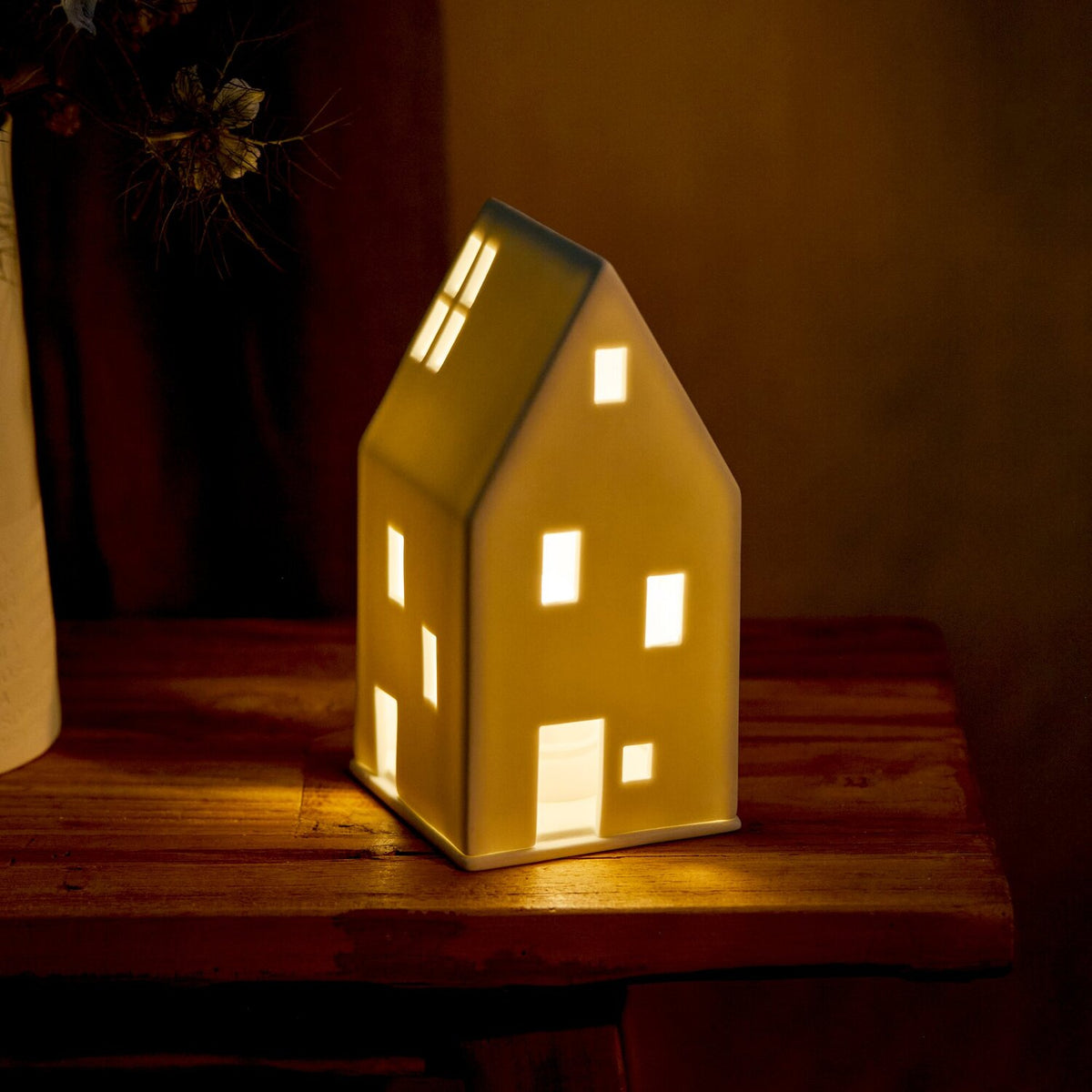 Weißes Lichthaus mit Satteldach, warm erleuchtete Fensteröffnungen und Dachbereich