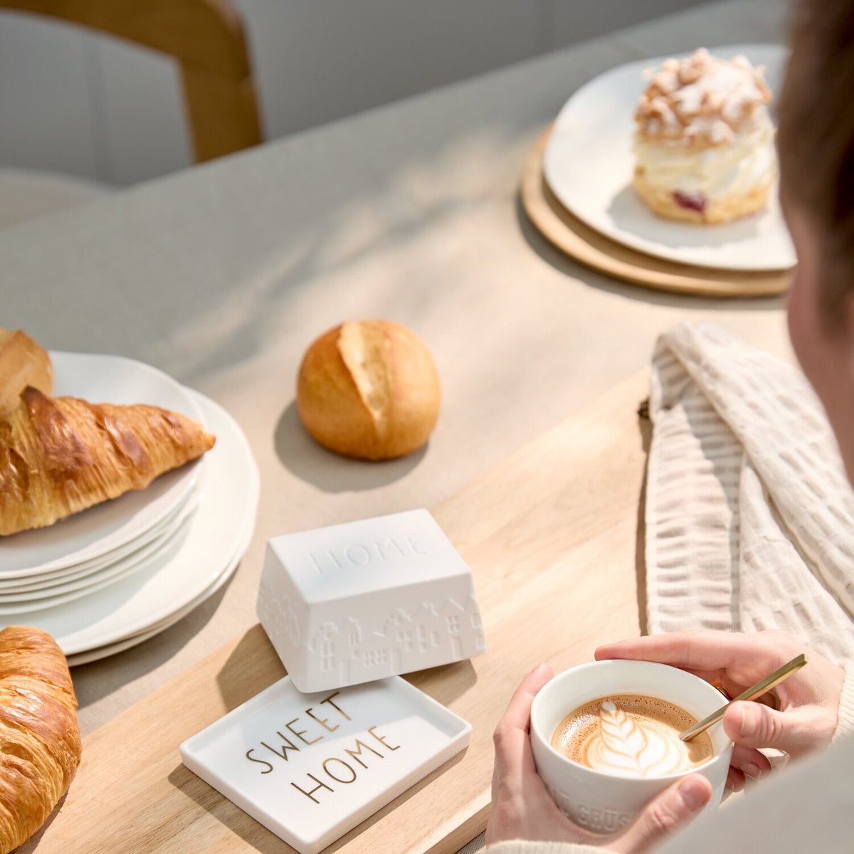 Butterdose „SWEET HOME“ auf Holzbrett beim Frühstück, Tasse mit Milchschaum daneben