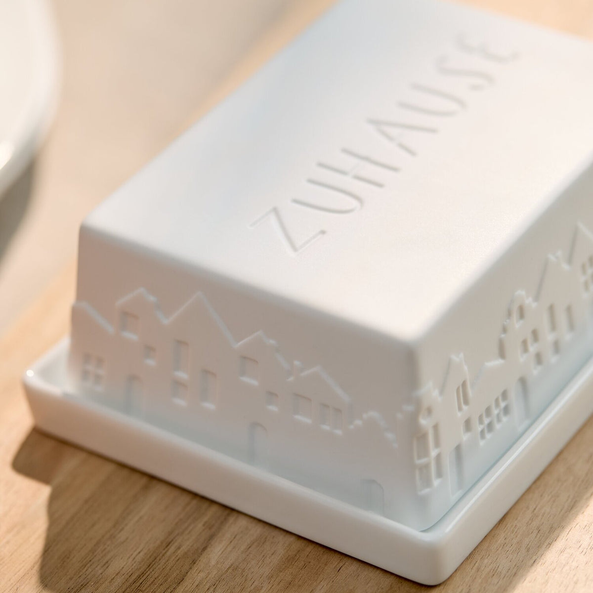 Weiße Butterdose mit erhabenem „ZUHAUSE“-Schriftzug auf dem Deckel und Stadtmotiv