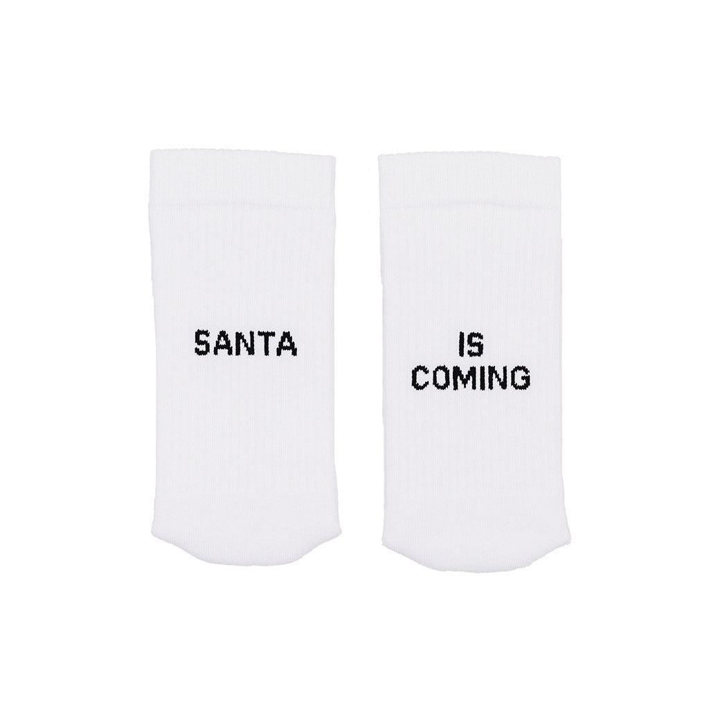 Weiße Socken mit Aufdruck „SANTA“ und „IS COMING“.