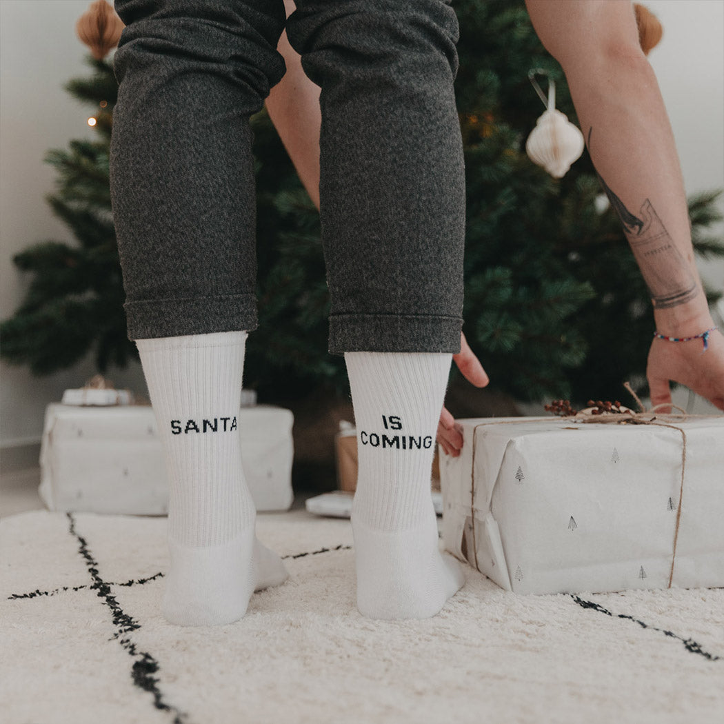 Weiße Socken am Fuß mit Aufdruck „SANTA“ und „IS COMING“.