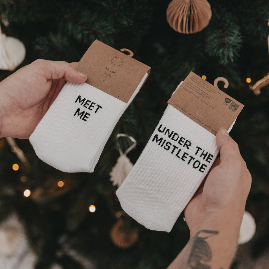 Zwei weiße Socken in Packungen, „MEET ME“ und „UNDER THE MISTLETOE“