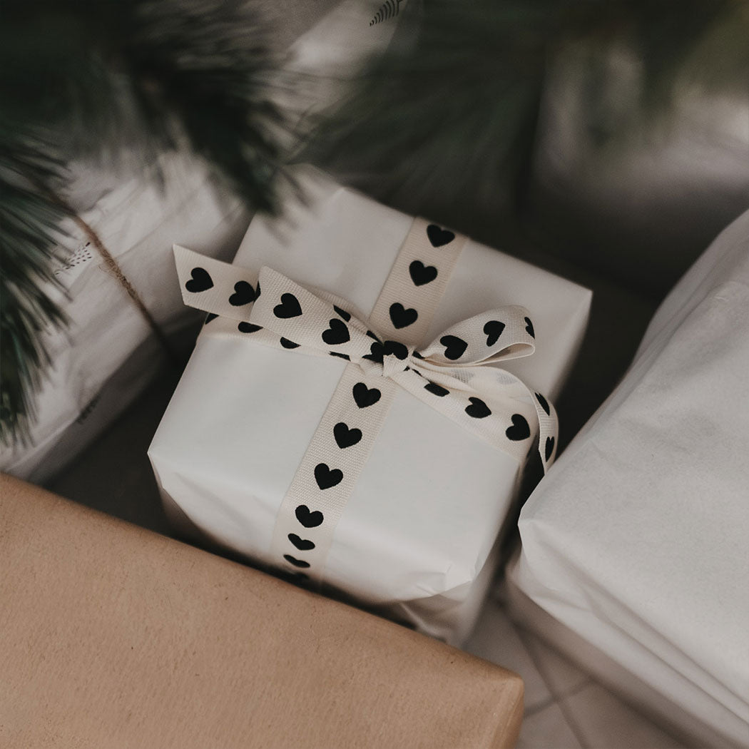 Geschenkband mit Herzen als Schleife auf weißem Geschenkpapier