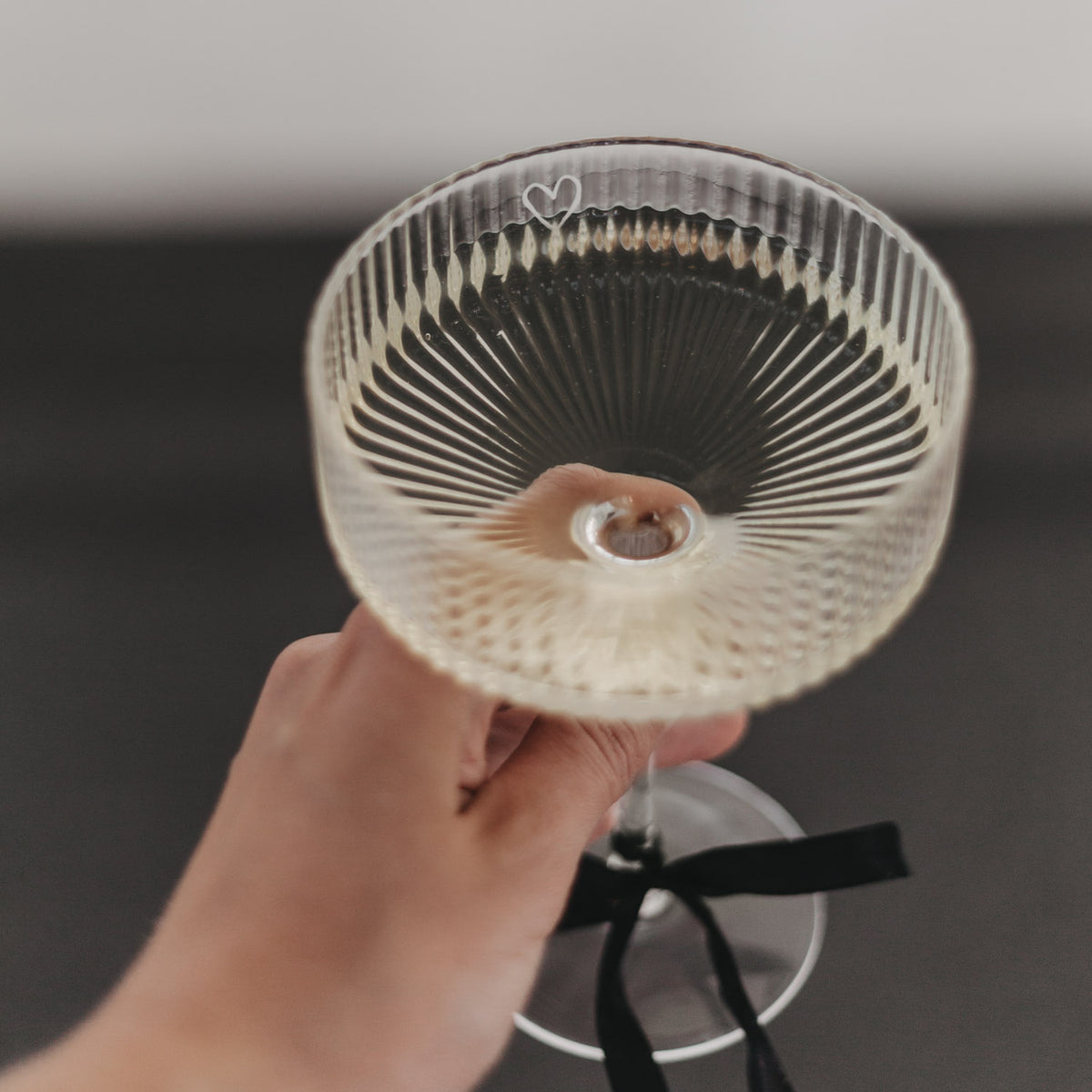 Champagnerglas mit Herzgravur, transparent, Blick von oben, schwarze Schleife am Stiel