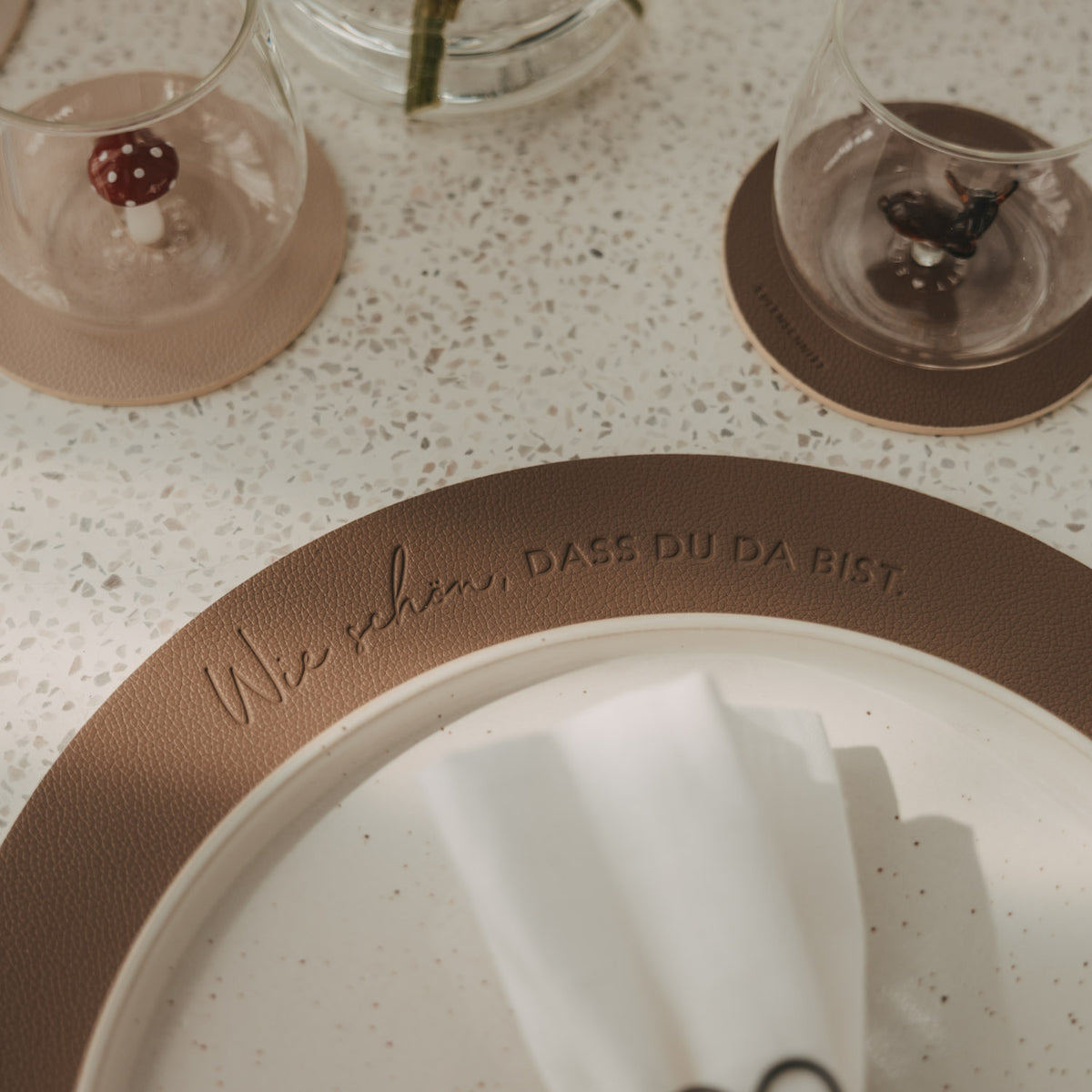 Platzset braun mit eingeprägtem Schriftzug, gefaltete Serviette darauf