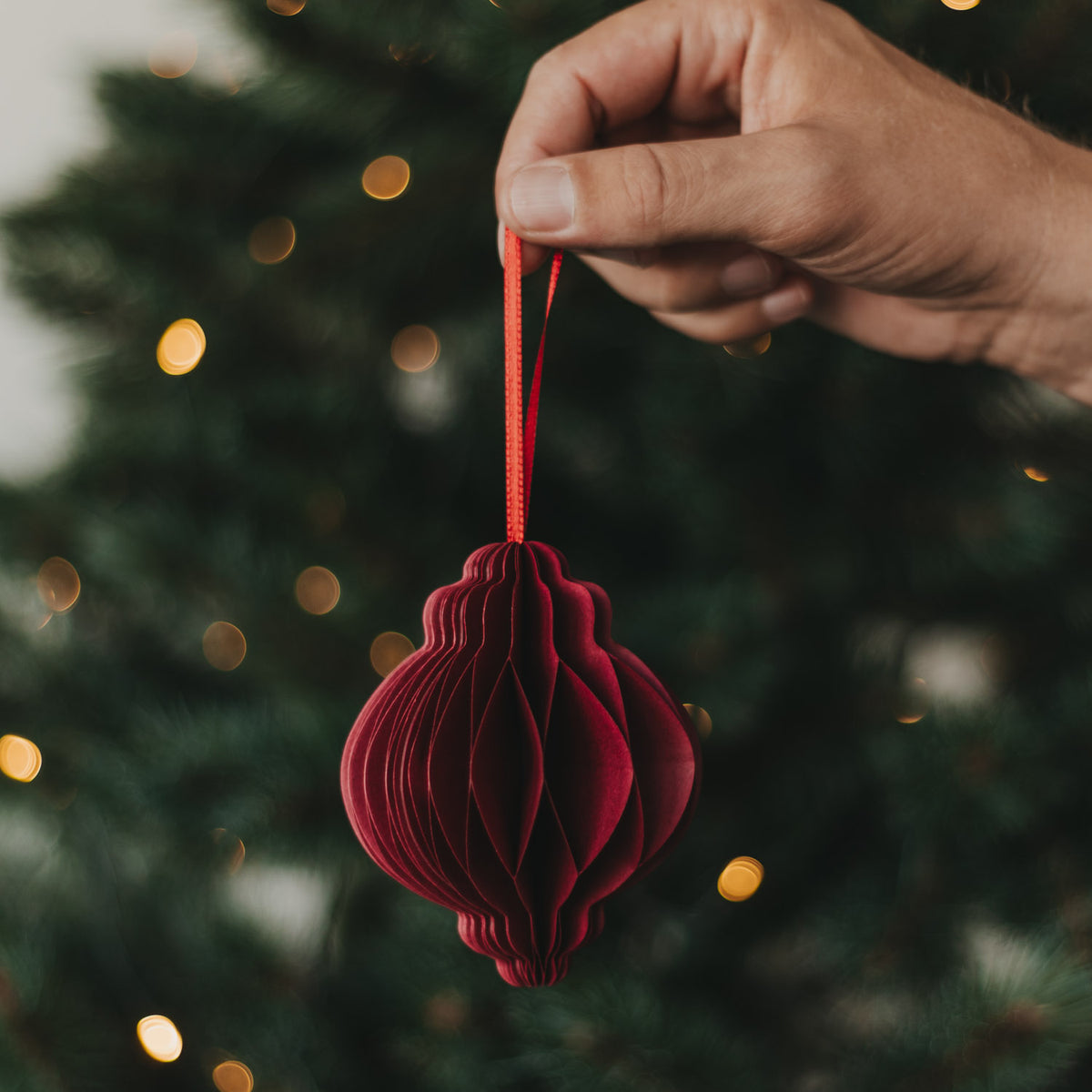 Roter Papieranhänger, von Hand an roter Schlaufe gehalten, gefaltete Kugelform