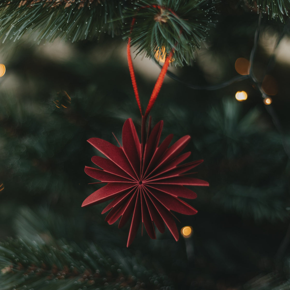 Dunkelroter Papieranhänger „Schneeflocke“ rundes Faltendesign, hängend am Tannenast