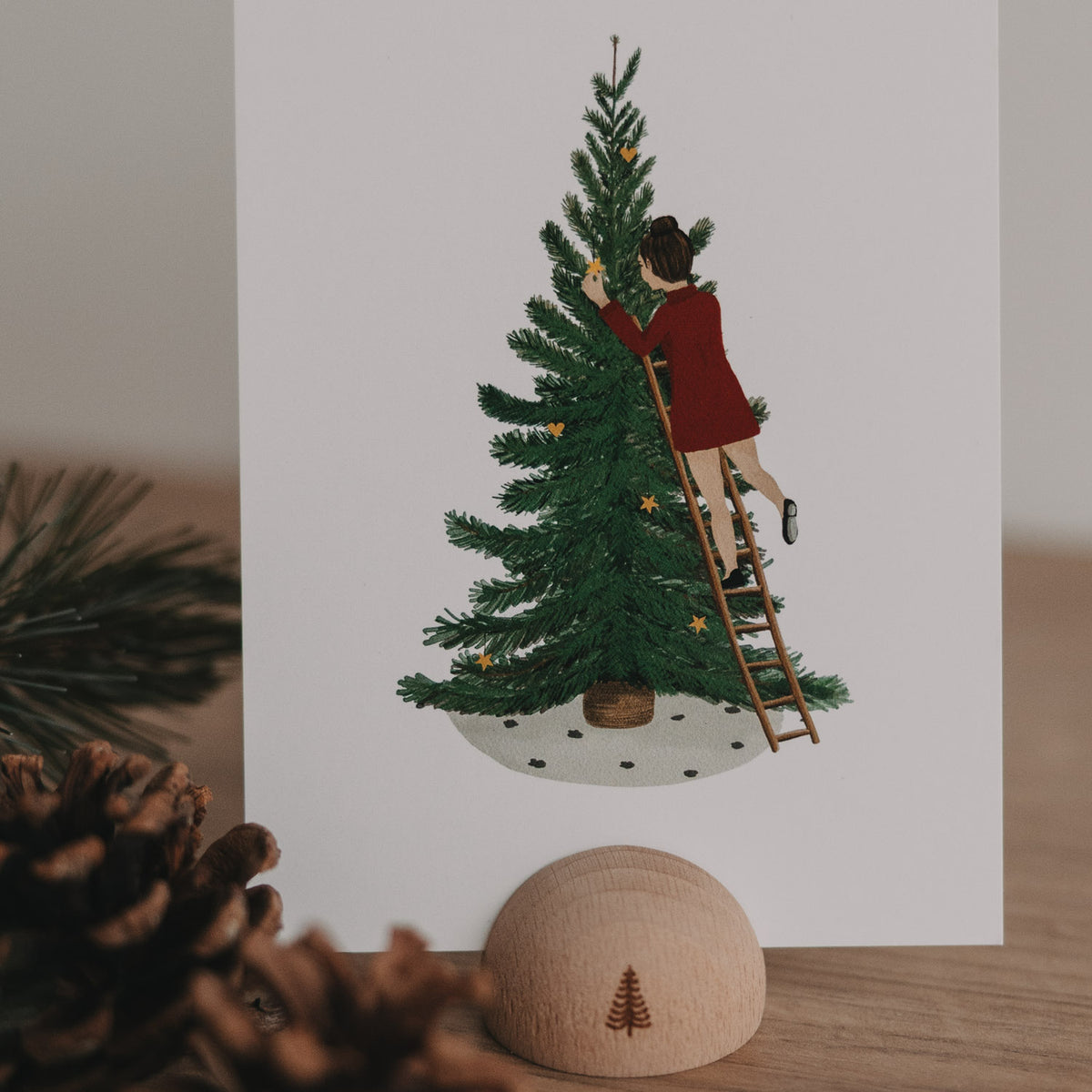 Aquarellkarte mit Mädchen am Leiter neben Tannenbaum und Schneefläche