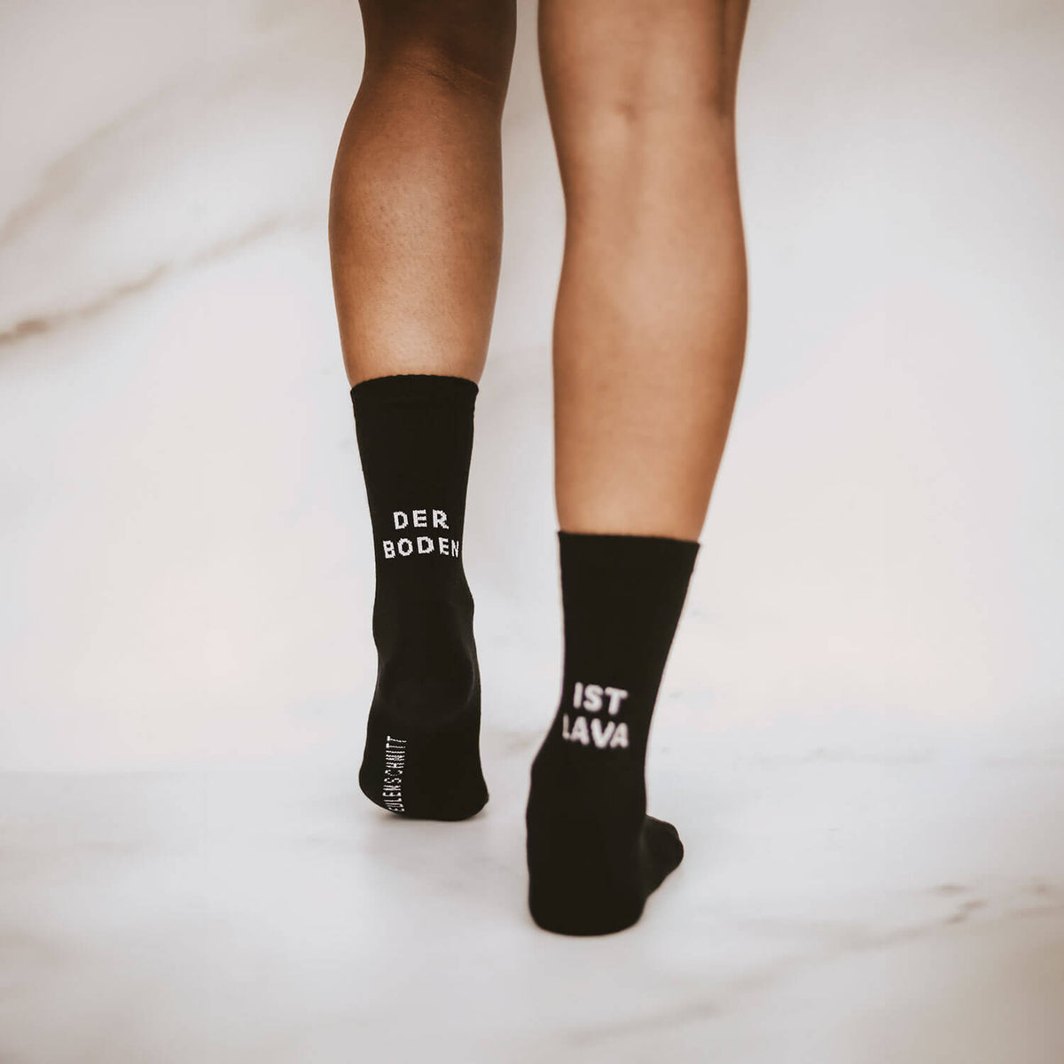 Schwarze Socken am Knöchel, „DER BODEN“ links und „IST LAVA“ rechts