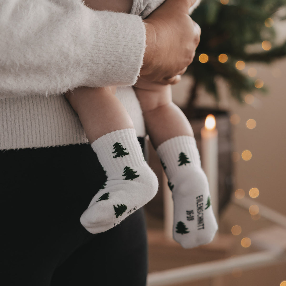Babysocken in Weiß mit grünen Tannen, Vorderansicht am Fuß
