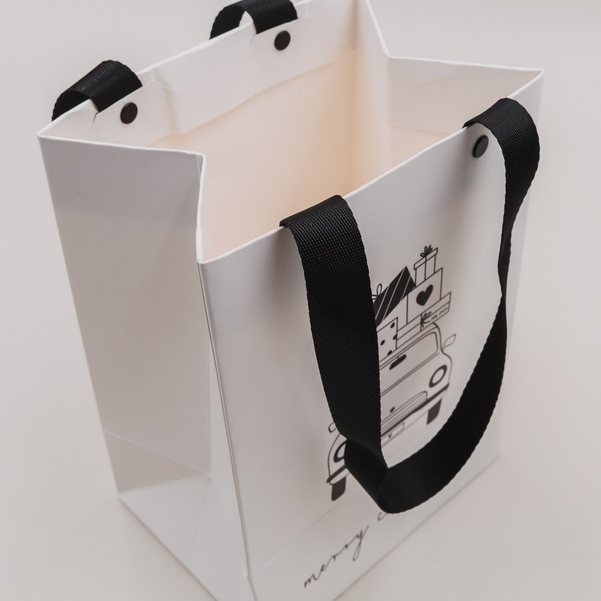 Weiße Geschenktüten geöffnet; innen sichtbar, mit schwarzem Trageband und Weihnachtsauto-Motiv.
