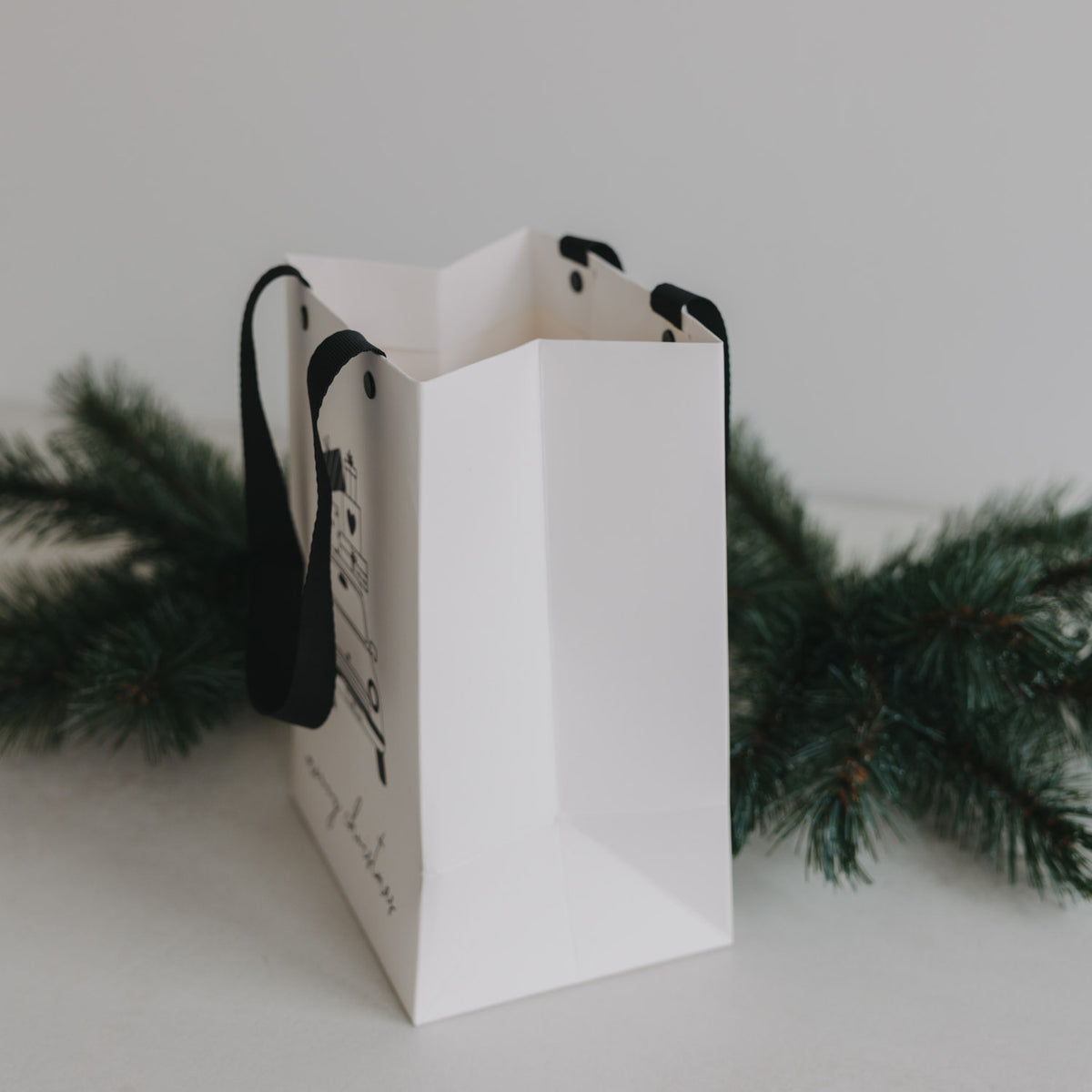 Weiße Geschenktüte mit schwarzem Trageband; Seitenansicht mit Weihnachtsauto-Design.