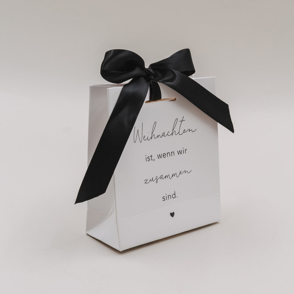Weiße Geschenktüte mit großer schwarzer Schleife und Aufdruck „Weihnachten ist, wenn wir zusammen sind.“