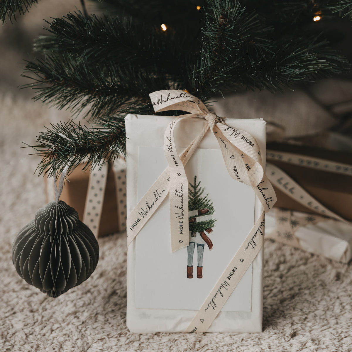 Geschenkband um ein weißes Päckchen, „FROHE WEIHNACHTEN“ sichtbar