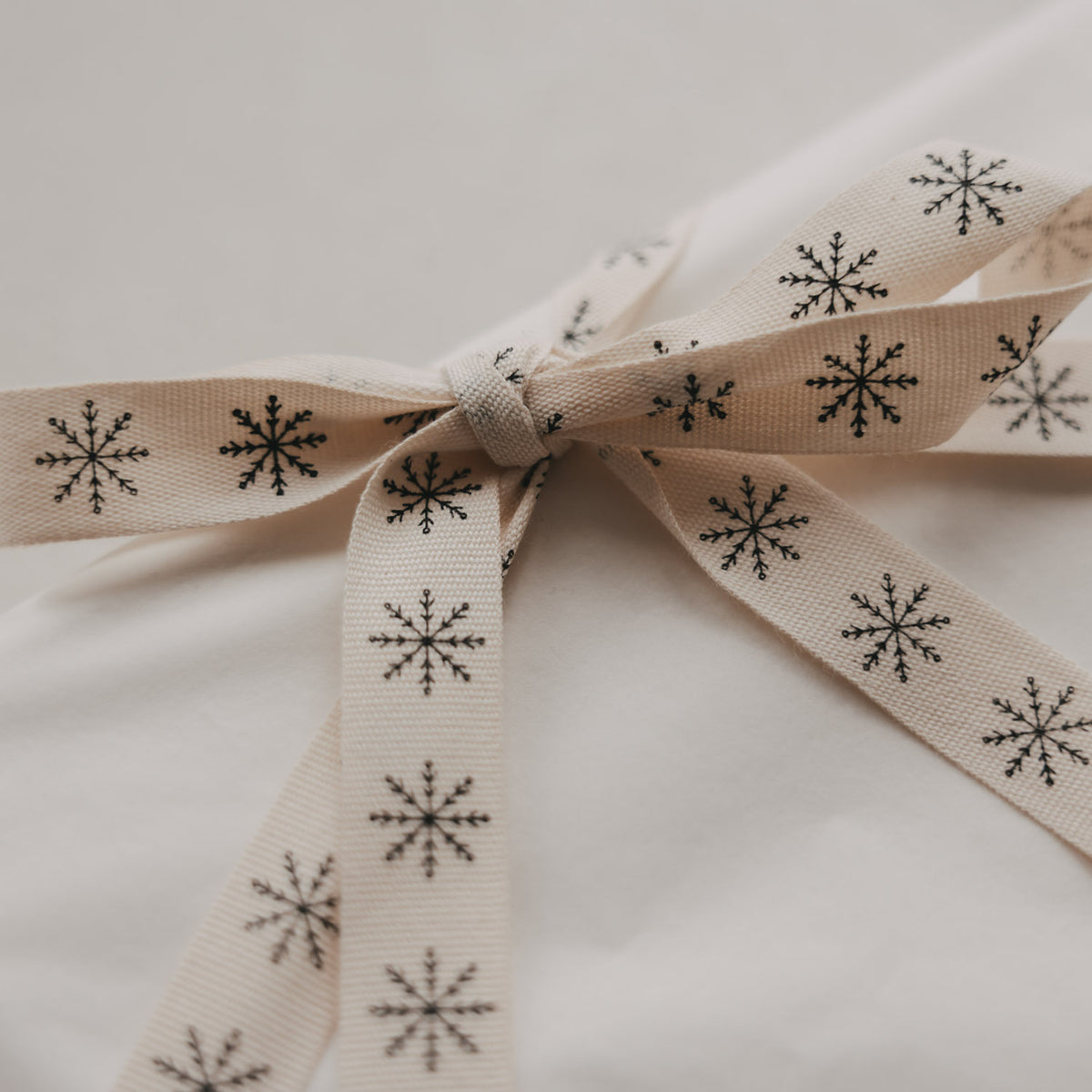 Detail der Schleife: beiges Geschenkband mit kleinen Schneeflocken, Stoffband in Nahaufnahme