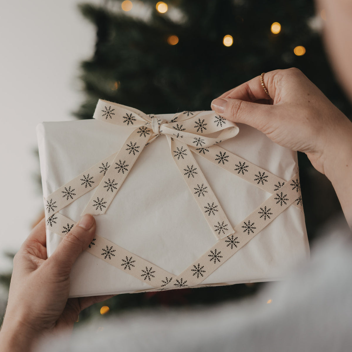 Geschenkband mit Schleife, beiger Stoff mit schwarzen und grauen Schneeflocken, in Händen